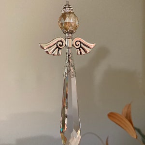 May include: A crystal angel suncatcher with a clear teardrop-shaped crystal and a gold-toned metal angel with wings. The angel has a round, faceted crystal in the center.