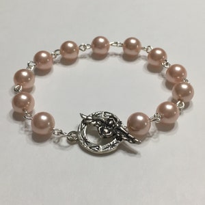 May include: A delicate bracelet made with pale pink pearls and a silver toggle clasp featuring a floral design.