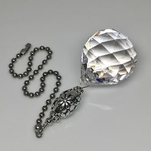May include: A clear crystal ball with a silver chain and a silver bead with a floral design. The crystal ball is faceted and reflects light.