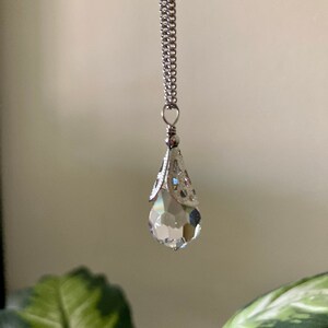 May include: A silver chain necklace with a clear crystal teardrop pendant. The pendant has a silver filigree design around the top.