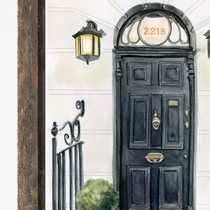 May include: A black door with a gold door knocker and a brass mailbox. The door has a rounded archway with the number "221B" above it. A black wrought iron gate with a decorative top is to the left of the door. A small green bush is in front of the door.