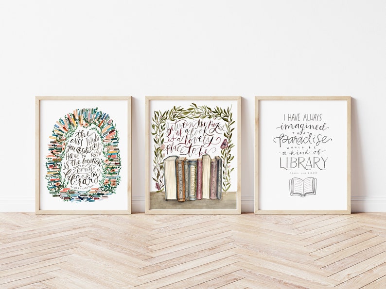 May include: Three framed prints with watercolor illustrations of books and text about libraries. The first print features a circle of books with the text "the only thing you absolutely have to know is the location of the library". The second print features a stack of books with a leafy border and the text "between the pages of a book is a lovely place to be". The third print features an open book with the text "I have always imagined paradise a kind of library".
