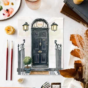 May include: A watercolor painting of a black door with a gold number "221B" above it. The door is surrounded by a white frame and has a small window above it. There are two black lanterns on either side of the door. The painting is on a white background.