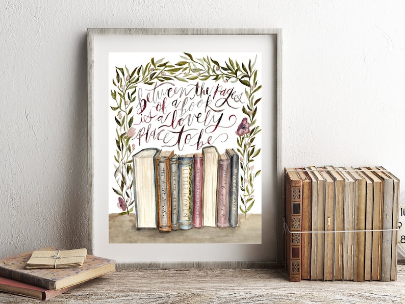 May include: A framed watercolor print with a quote about books: "Between the pages of a book is a lovely place to be." The quote is surrounded by a wreath of green leaves and pink flowers. A row of vintage books are displayed below the quote.