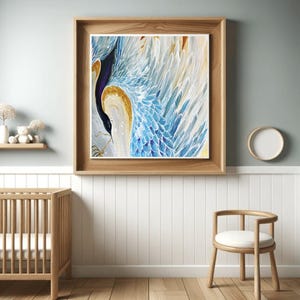 May include: A framed artwork featuring a stylized bird with blue and white wings, a black body, and gold accents. The artwork is displayed in a light wood frame, hanging on a light blue wall. The room also includes a wooden crib, a small shelf with decor, and a wooden chair.