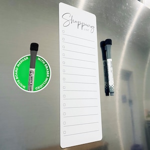 Könnte beinhalten: Weiße magnetische Einkaufsliste mit 15 Zeilen und dem Text "Shopping List" oben. Zwei graue Trockenlöschmarker sind an der Liste befestigt.
