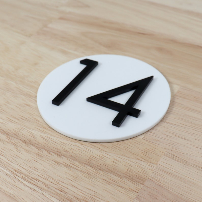 May include: White round sign with the number 14 in black raised lettering.