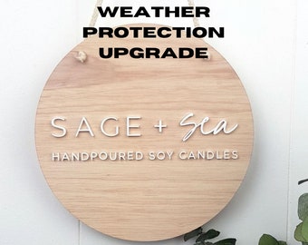 May include: A round wooden sign with the text "WEATHER PROTECTION UPGRADE" at the top and "SAGE + Sea HANDPOURED SOY CANDLES" at the bottom.