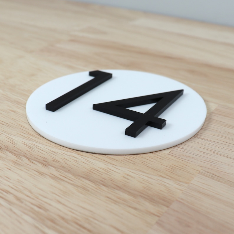May include: White circular sign with black numbers "14" on a wooden surface.
