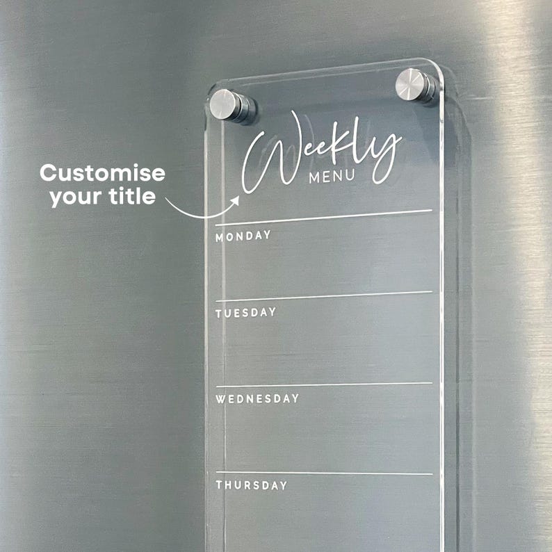 May include: A clear acrylic weekly menu board with a white inscription that says "Weekly Menu". The board has a space for each day of the week, Monday through Thursday, with lines for writing in meals.