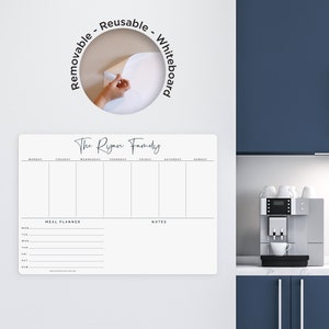 Puede incluir: Pizarra blanca rectangular con el texto "The Ryan Family" y un diseño de planificador de comidas semanal. La pizarra está etiquetada como "Removable - Reusable - Whiteboard". Una mano despega la pizarra de la pared.