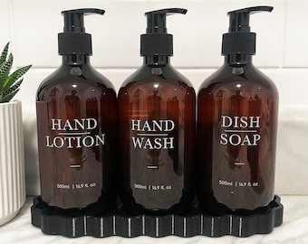 Può includere: Tre flaconi in vetro ambrato con erogatori a pompa neri, etichettati in bianco con le scritte Hand Lotion, Hand Wash e Dish Soap. Ogni flacone ha una capacità di 500 ml e poggia su un vassoio nero rettangolare dai bordi smerlati.
