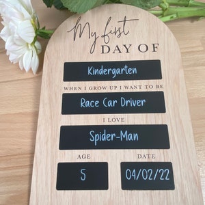 Puede incluir: Un letrero de madera con el texto "My first day of Kindergarten" y un fondo de pizarra. El letrero tambi&eacute;n incluye la edad del ni&ntilde;o, la fecha, su superh&eacute;roe favorito y lo que quiere ser cuando sea mayor.