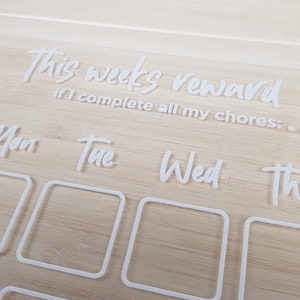 May include: White acrylic chore chart with the text "this week's reward if I complete all my chores:". The chart has seven days of the week labeled: Mon, Tue, Wed, Thu, Fri, Sat, Sun. Each day has a square for checking off chores.