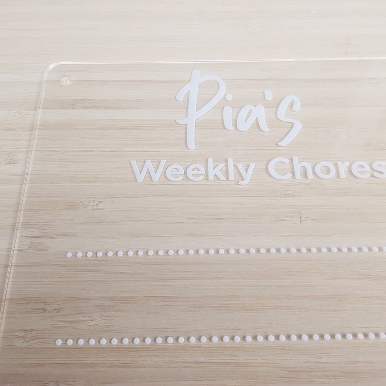 May include: A clear acrylic sign with the text "Pia's Weekly Chores" in white lettering. The sign has two rows of small white dots.