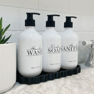 May include: Three white pump bottles with black labels and lids on a black wavy tray. The labels read "Hand Wash", "Dish Soap", and "Hand Sanitizer". Each bottle contains 500 ml or 16.9 fl oz.