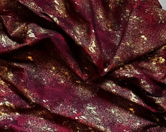 May include: Burgundy fabric with a gold metallic print. The fabric has a subtle shimmer and a textured feel.