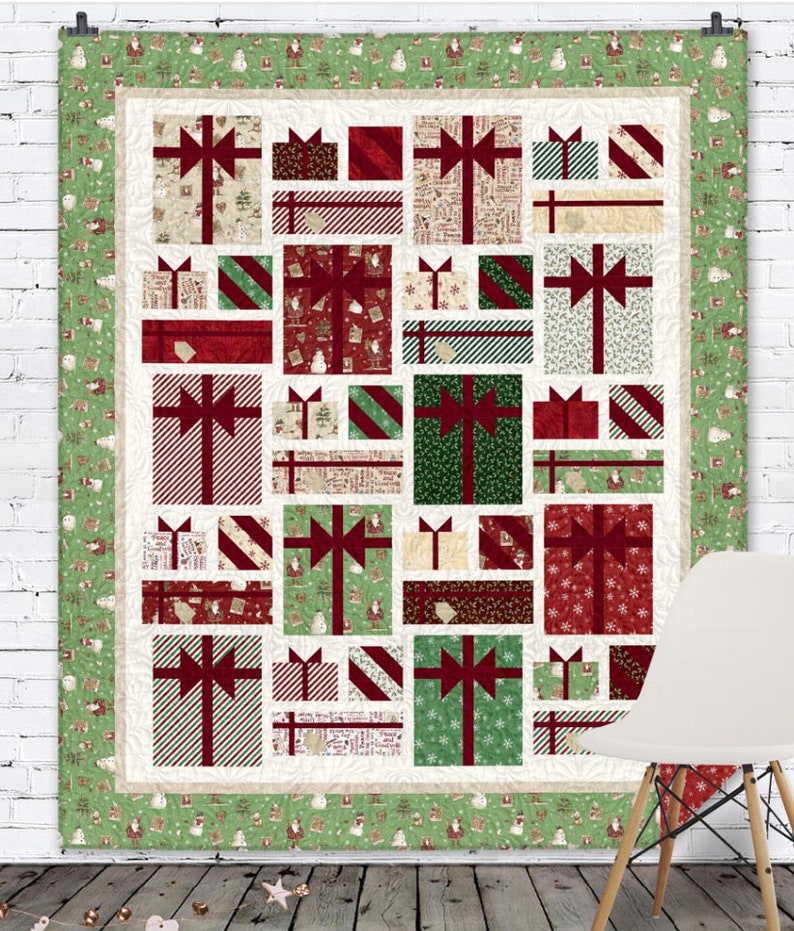 May include: A Christmas quilt with a patchwork design of presents in various colors and patterns. The quilt is framed with a green border featuring a repeating pattern of snowmen and Santa Claus.