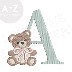 Puede incluir: Diseño bordado con la letra "A" en azul claro con textura tejida, acompañado de un oso de peluche marrón con un lazo rosa. Parte de una colección completa del alfabeto.