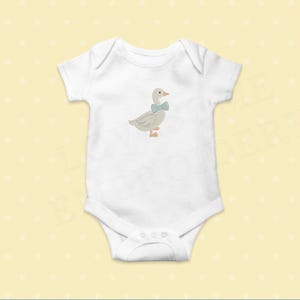 May include: White baby onesie with a light gray embroidered goose wearing a blue bow tie. The goose has an orange beak and feet. The onesie has short sleeves and a snap closure at the bottom. The background is a light yellow color.