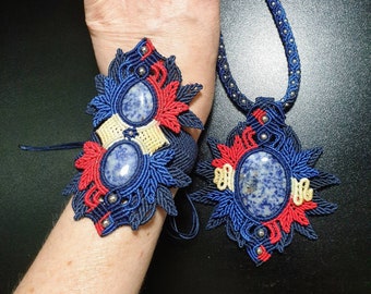 May include: A macrame bracelet and matching necklace set featuring dark blue, red, and cream-coloured cord woven into intricate patterns. Each piece contains a smooth, oval-shaped blue and white speckled stone accented with small silver-toned beads.