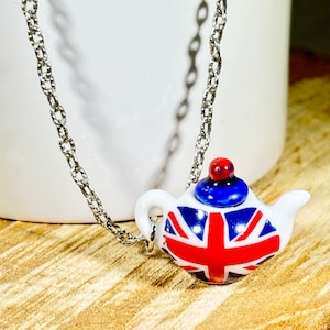 May include: A silver chain necklace with a small white teapot pendant. The teapot is decorated with the Union Jack flag in red, white, and blue.