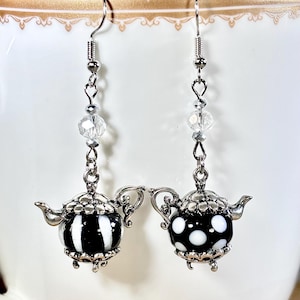 May include: A pair of silver teapot earrings with black and white striped and polka dot glass charms. The earrings have clear crystal beads and silver hooks.