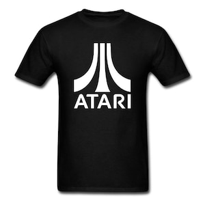 Könnte beinhalten: Schwarzes T-Shirt mit dem weißen Atari-Logo. Das Logo besteht aus drei weißen vertikalen Linien, die sich oben nach innen krümmen, mit dem Wort "ATARI" darunter in einer fetten, serifenlosen Schrift.
