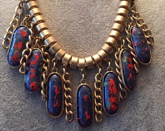 May include: A gold chain necklace with multiple blue and red oval-shaped pendants. The pendants have a marbled effect with red and blue paint.