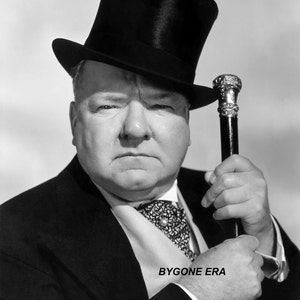 May include: A black and white photo of a man wearing a black top hat and a suit. He is holding a cane in his right hand.