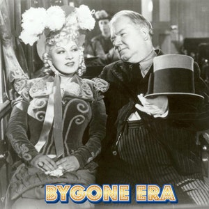 May include: A black and white photo of a woman wearing a large, feathered hat and a man wearing a top hat. The woman is sitting in a train car and the man is standing next to her. The photo has the text "Bygone Era" printed at the bottom.