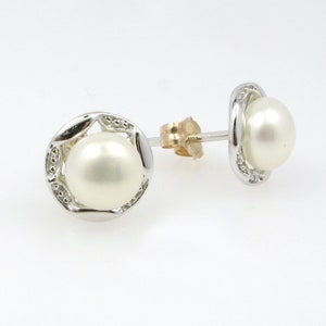 May include: A pair of pearl earrings with a silver setting. The pearls are white and round. The earrings have a simple design.