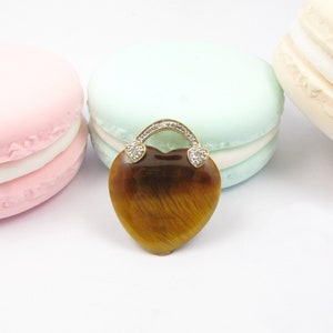 May include: A heart-shaped pendant with a tiger's eye stone set in gold. The pendant is surrounded by small diamonds and has a gold chain.