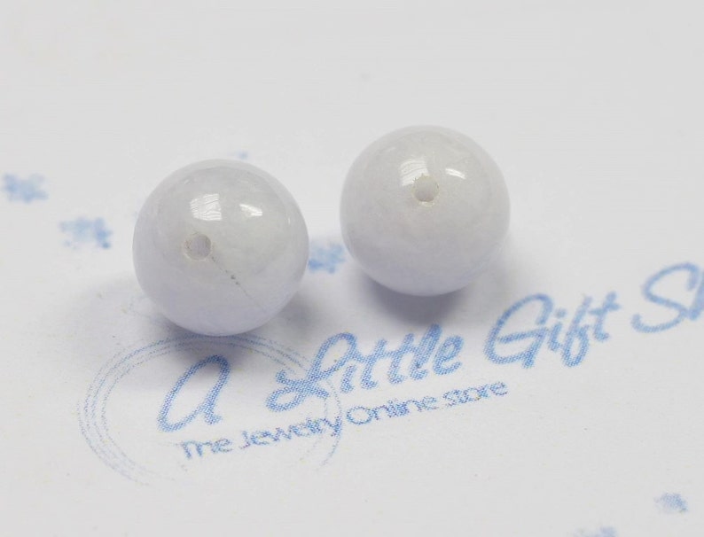 May include: Two light blue round beads with a hole in the center. The beads are smooth and have a slight shine.