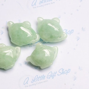 Könnte beinhalten: Fünf jadegrüne Teekannen-Anhänger, jeder mit einer leicht unterschiedlichen Form und Größe. Die Anhänger sind aus glattem, poliertem Jade gefertigt und haben eine hellgrüne Farbe.