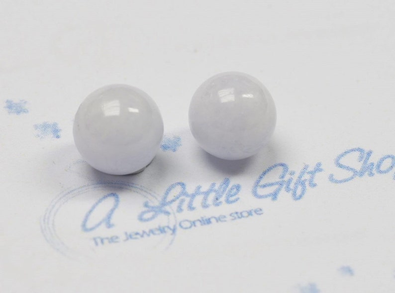 May include: Two white, round, smooth, polished beads. The beads are slightly translucent and have a subtle sheen.