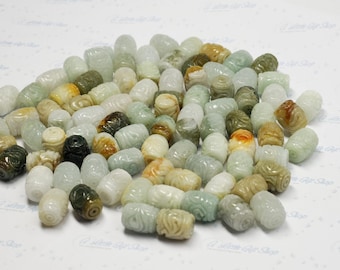 May include: A large collection of cylindrical beads carved from natural stone in various shades of pale green, white, tan, and dark olive. Each bead features a detailed, repeating floral or scroll pattern etched into the surface.