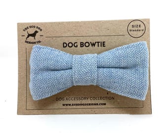 May include: A light blue herringbone patterned dog bow tie on a brown card with the text "The Eco Dog Design Co." and "Dog Bowtie". The card also includes the text "Size Standard" in a circle.