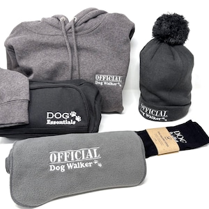 May include: A selection of dog-themed merchandise, including a grey hoodie, a black wash bag, a grey beanie hat with a bobble, a grey fleece blanket, and a pair of black socks. The items display the text "OFFICIAL Dog Walker" and "DOG Essentials".