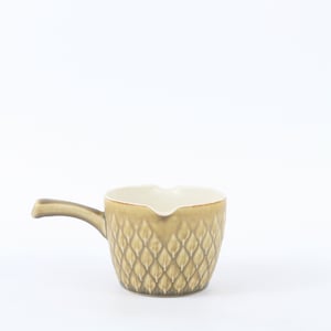 Può includere: Una piccola salsiera in ceramica color marrone chiaro con un manico. L'esterno presenta un motivo strutturato a forma di diamante. L'interno è color crema. La salsiera è progettata per servire salse.