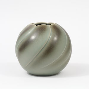 Peut inclure: Un vase en céramique vert avec un motif tourbillonnant et texturé. Le vase est rond et a une large ouverture.