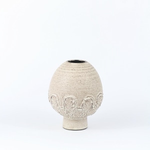 Peut inclure: Un vase en céramique beige avec un corps texturé en forme d'œuf et une base courte en piédestal. Le vase a un intérieur sombre et une bande décorative de motifs en forme de feuilles autour de la partie inférieure du corps. Le vase mesure environ 20 cm de haut.
