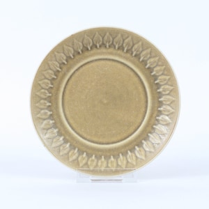 Könnte beinhalten: Ein hellbrauner Teller aus Keramik mit einem dekorativen Rand aus stilisierten Blättern. Der Teller hat eine leicht strukturierte Oberfläche.