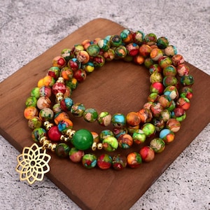 May include: Multi-strand beaded bracelet with a gold-tone pendant in the shape of a flower. The beads are small and round, and they are made of a variety of colors, including red, orange, yellow, green, blue, and purple.
