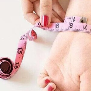 May include: A pink measuring tape wrapped around a person's wrist. The tape reads 6, 7, 8, and 9 inches.