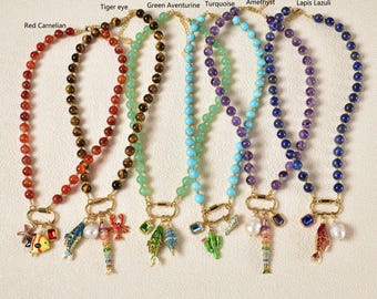 May include: Six beaded necklaces in red, brown, green, turquoise, purple, and blue. Each necklace features a gold clasp and a charm with a fish, lobster, or other sea-themed design. The necklaces are labelled with the stone type.