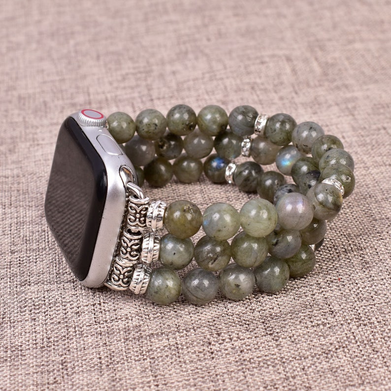 May include: A silver and green beaded watch band with a silver clasp. The band is made of multiple strands of beads and is designed to fit an Apple Watch.