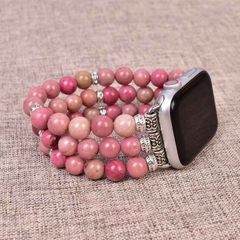 May include: A pink and silver beaded watch band with a silver clasp. The band is made of multiple strands of pink beads and has a silver clasp with a decorative design.