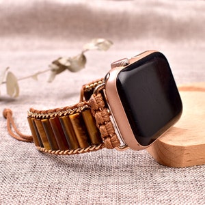 Pode incluir: Uma pulseira de relógio de couro marrom e olho de tigre para um Apple Watch. A pulseira tem um detalhe de corrente dourada e uma alça de couro marrom.