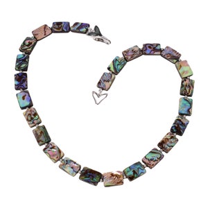 Puede incluir: Un collar hecho de cuadrados de concha de abulón iridiscente, con un cierre plateado en forma de corazón.